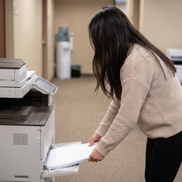 Lehrling im Büro nimmt Ausdrucke aus dem Drucker