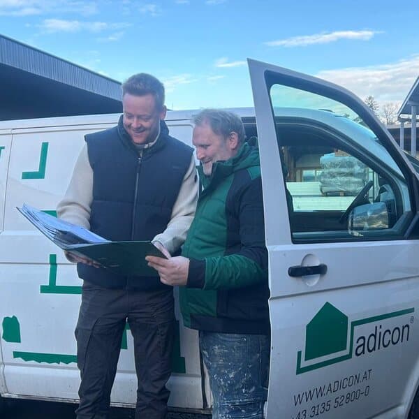 Zwei Mitarbeiter von adicon besprechen am Firmenwagen einen Plan