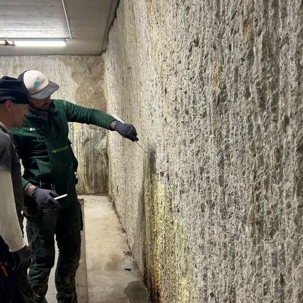 Zwei Mitarbeiter von adicon begutachten eine feuchte Betonwand