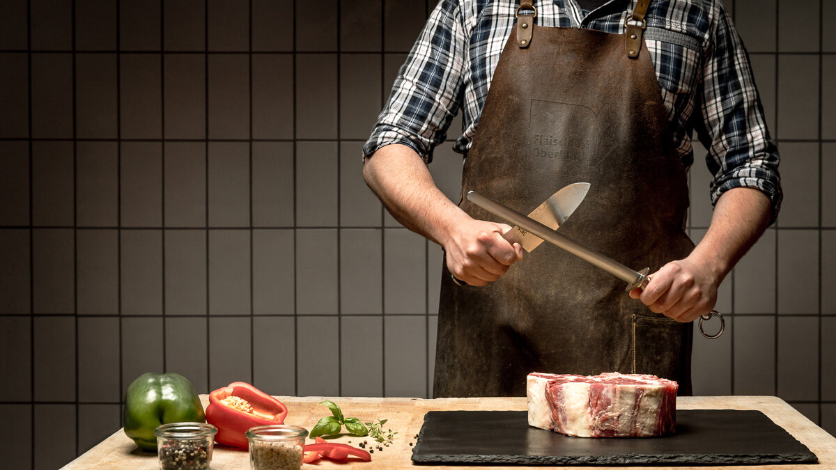 Metzger des Fleischhof Oberland schärft sein Messer vor einem Stück Fleisch