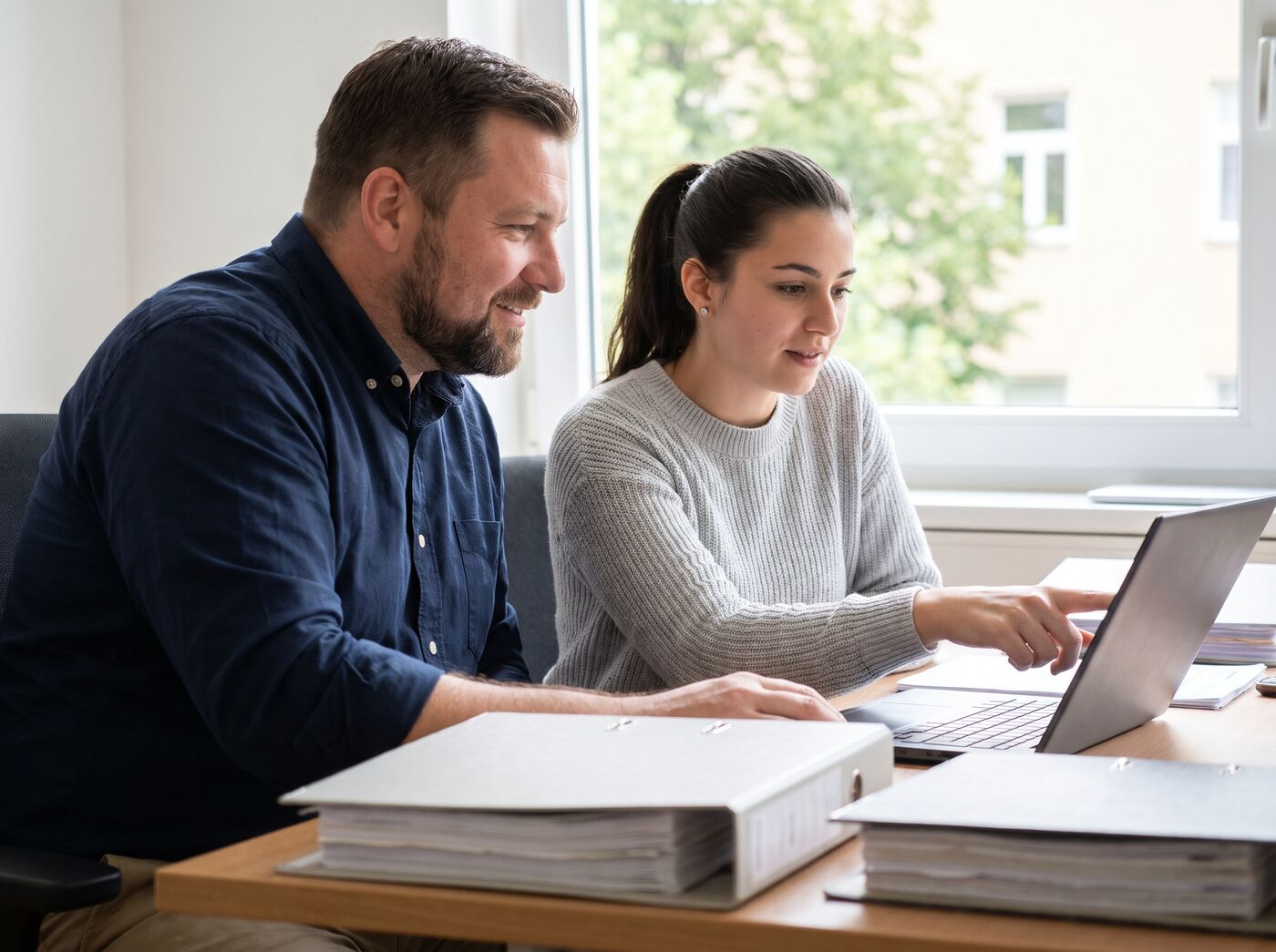 Geschäftsführer und eine Buchhalterin schauen im Büro gemeinsam auf einen Laptop